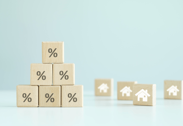 Wooden blocks with percent signs stacked beside house blocks, illustrating advertised mortgage rates vs your real rate