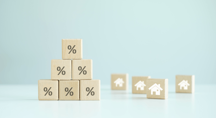 Wooden blocks with percent signs stacked beside house blocks, illustrating advertised mortgage rates vs your real rate